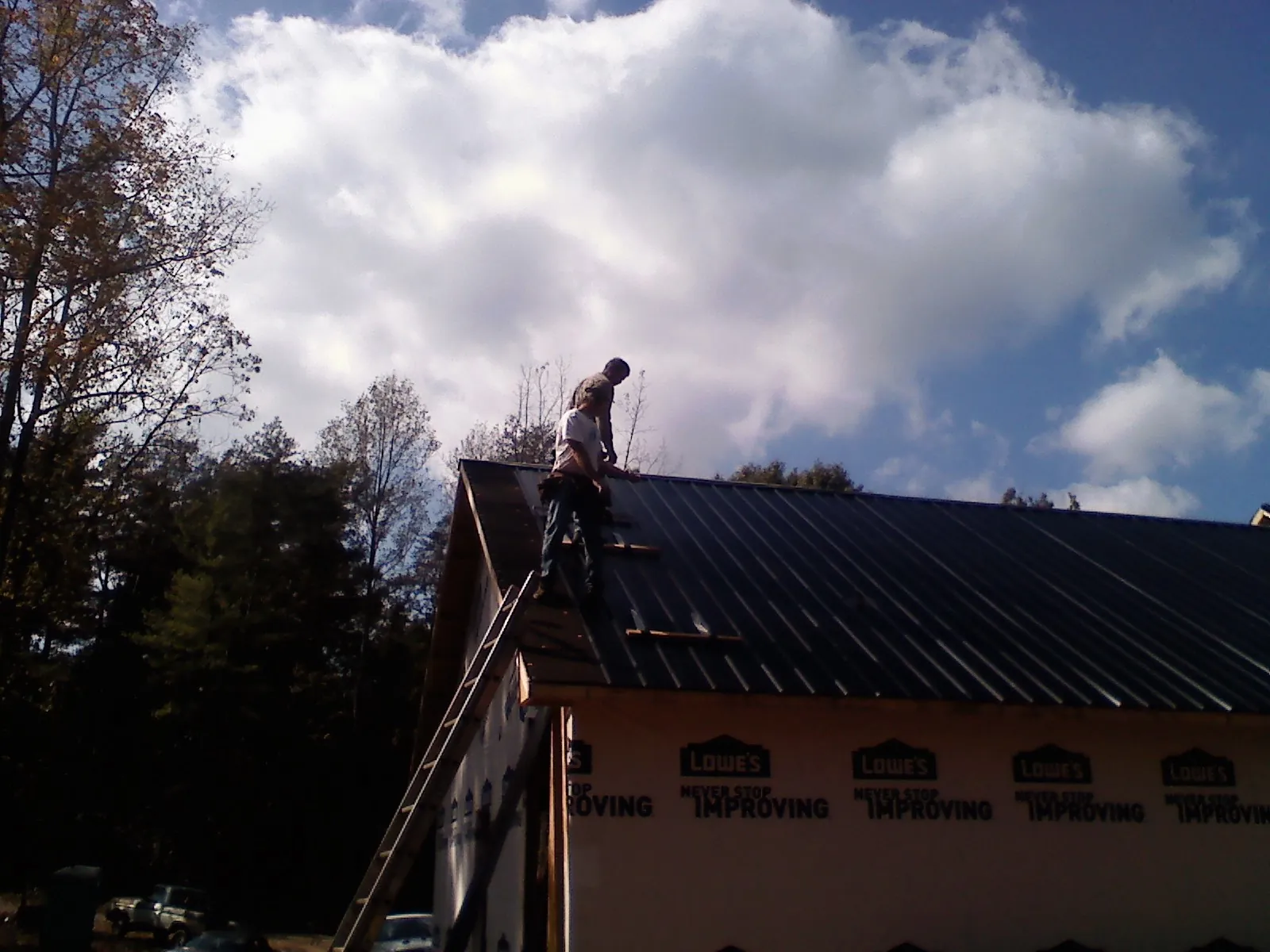 Roofer fastening dark metal panels high against a cloudy sky, from a Roof Inspection job in Bothell